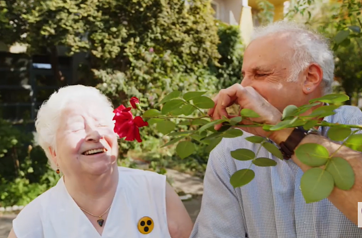 Eine blinde Frau riecht an einer roten Rose.
