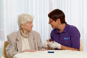 Pflegerin erklärt älterer Dame, wie sie den Zuckerwert misst.