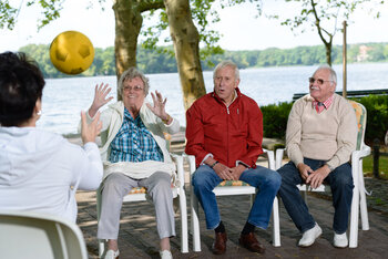 Drei ältere Menschen spielen mit einer Pflegerin Ball.