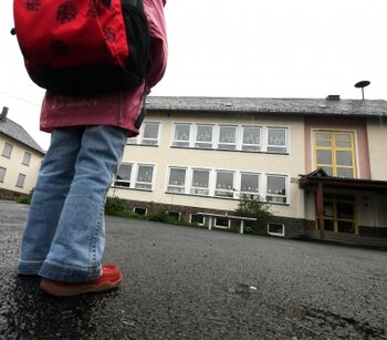 Ein Schulkind steht auf einem menschenleeren Schulhof vor einer Schule