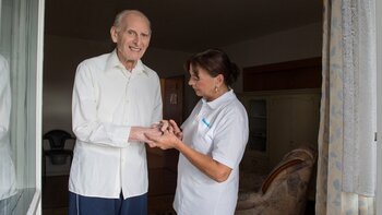 Pflegerin hilft alte Mann beim Eincremen der Hände.